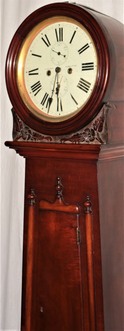 fig 1. A Victorian flame mahogany drumhead longcase clock featuring a circular hood, Roman numeral dial, and a tapered trunk flanked by turned columns.