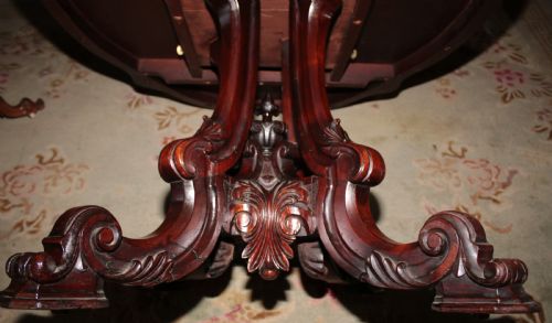 fig 1. A Victorian rosewood tilt-top dining table set vertically to reveal its dark figured grain pattern and scalloped serpentine top resting on a carved tripod base.
