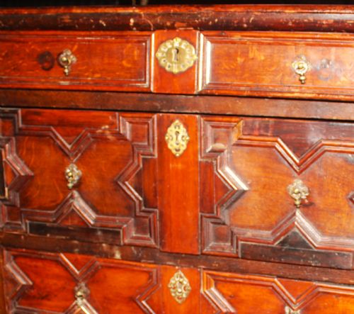 fig 1. A late seventeenth-century dark oak chest of four drawers featuring raised geometric panel mouldings and brass drop handles.