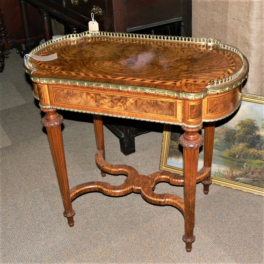 A burr walnut occasional table featuring a pierced brass gallery rail, geometric parquetry inlay, four tapered fluted legs, and an intricate X-form stretcher.