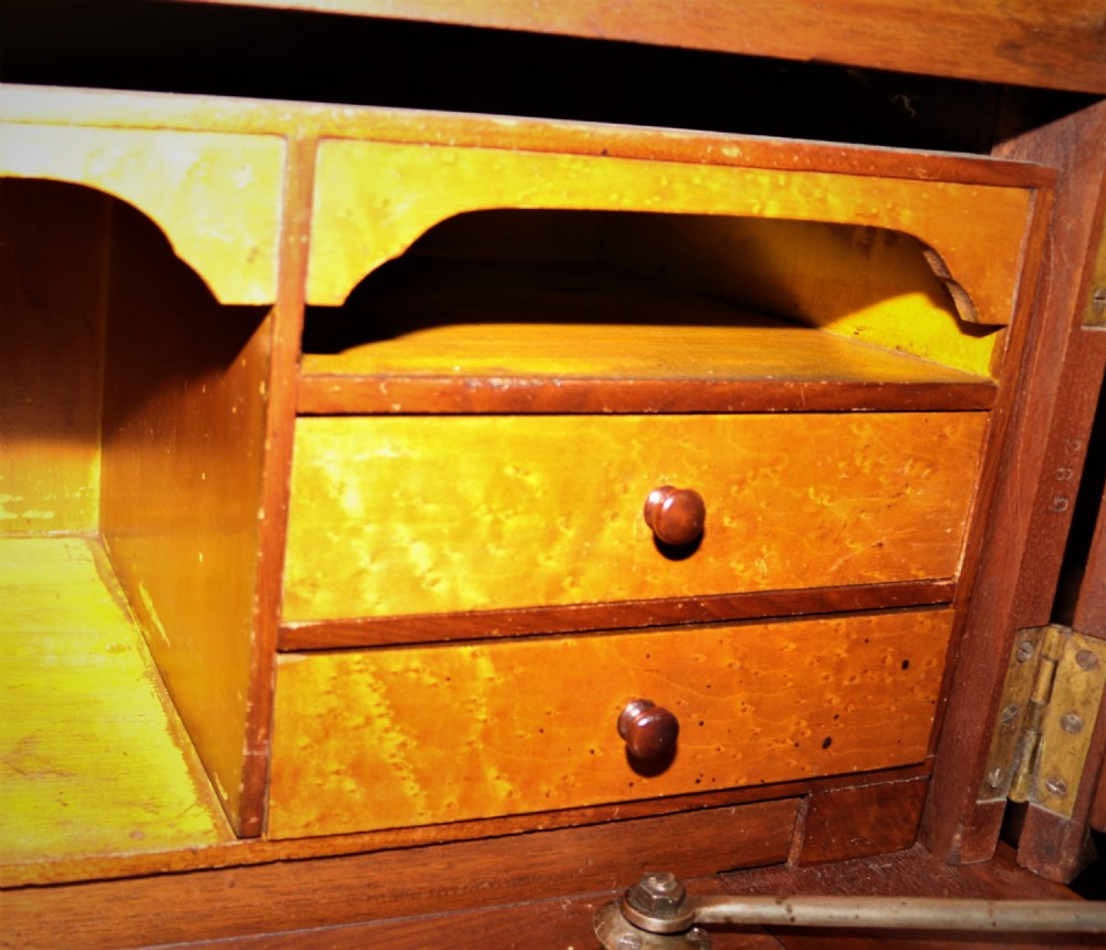 A Victorian walnut and maple cylinder desk featuring curved upper shutters, burr walnut panel inlays, a carved pediment, and double cabinet doors below. View VII