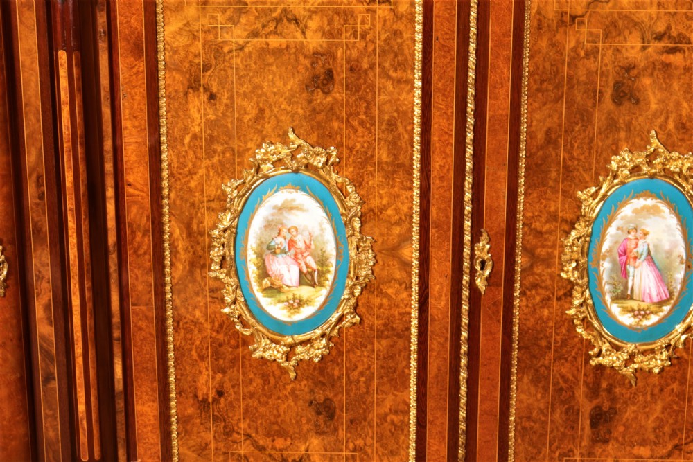 An antique Victorian burr walnut credenza featuring glazed end display doors, intricate marquetry inlay, gilt-metal mounts, and central cabinet doors adorned with oval painted porcelain plaques. View V