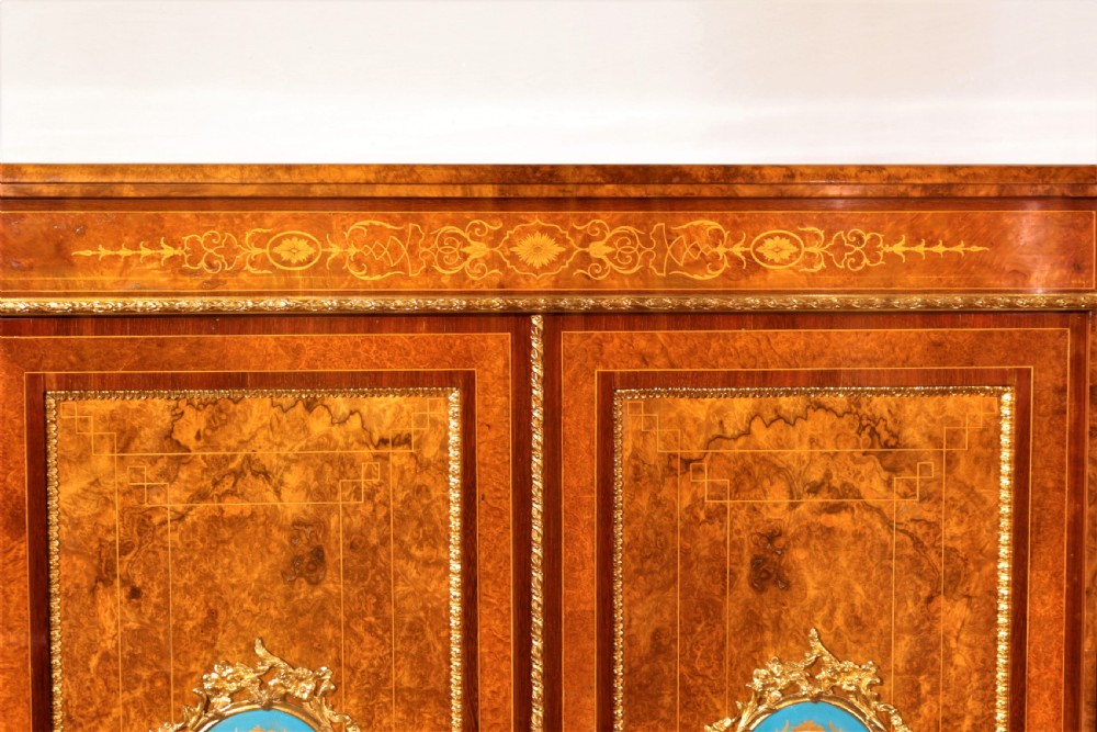 An antique Victorian burr walnut credenza featuring glazed end display doors, intricate marquetry inlay, gilt-metal mounts, and central cabinet doors adorned with oval painted porcelain plaques. View VI