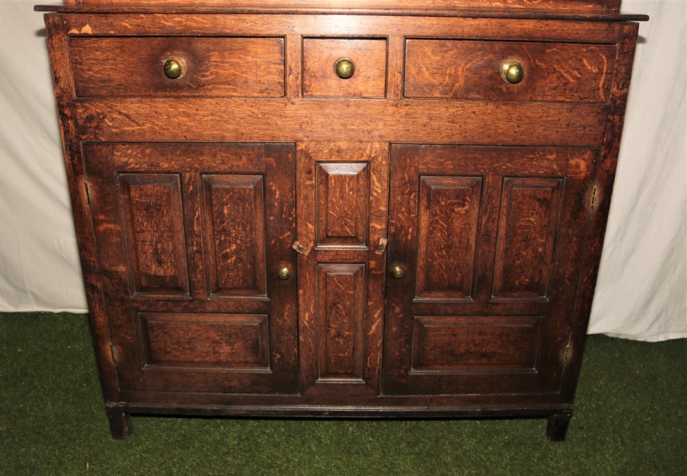 A dark oak court cupboard featuring arched panelled doors, drop finials, three middle drawers, and brass knobs. View II