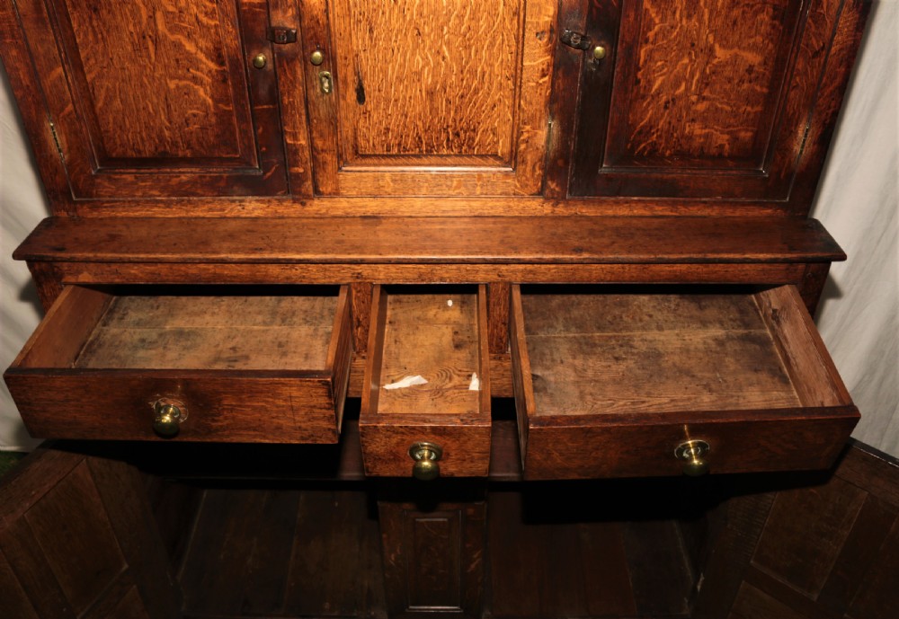 A dark oak court cupboard featuring arched panelled doors, drop finials, three middle drawers, and brass knobs. View VII
