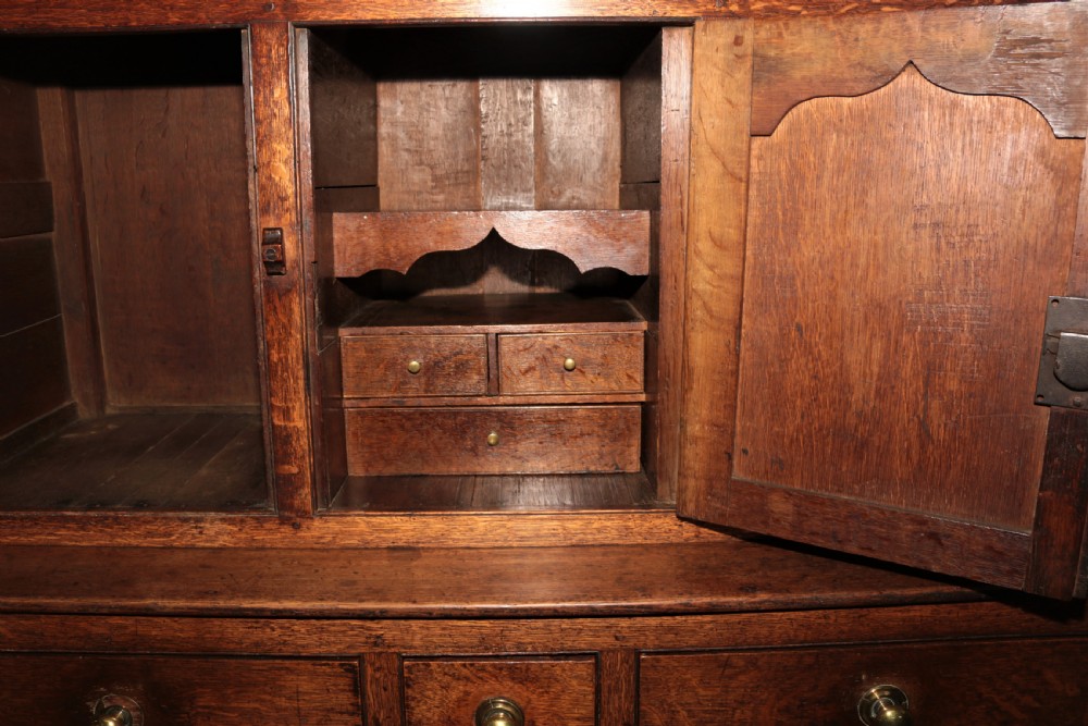 A dark oak court cupboard featuring arched panelled doors, drop finials, three middle drawers, and brass knobs. View XII
