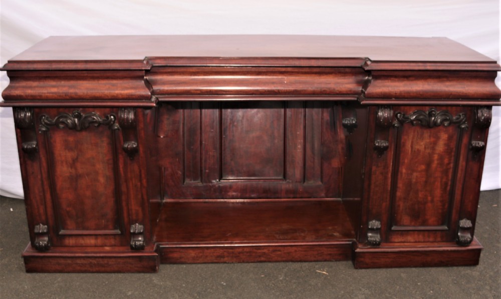 A Victorian dark mahogany sideboard featuring a large carved rococo backboard, flat serving surface, and two pedestal side cupboards. View VI