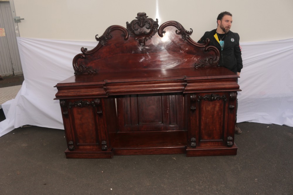 A Victorian dark mahogany sideboard featuring a large carved rococo backboard, flat serving surface, and two pedestal side cupboards. View X