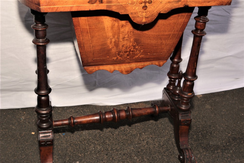 A Victorian burr walnut sewing table featuring decorative inlay, turned support legs, a lower storage well, and carved feet. View II