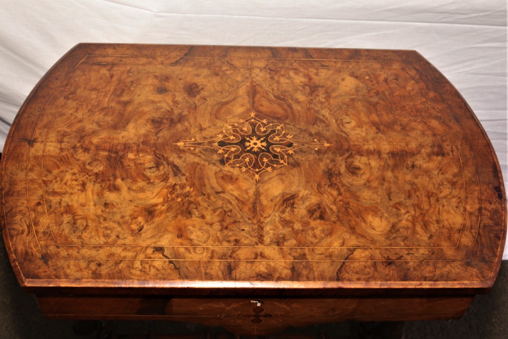 A Victorian burr walnut sewing table featuring decorative inlay, turned support legs, a lower storage well, and carved feet. View III