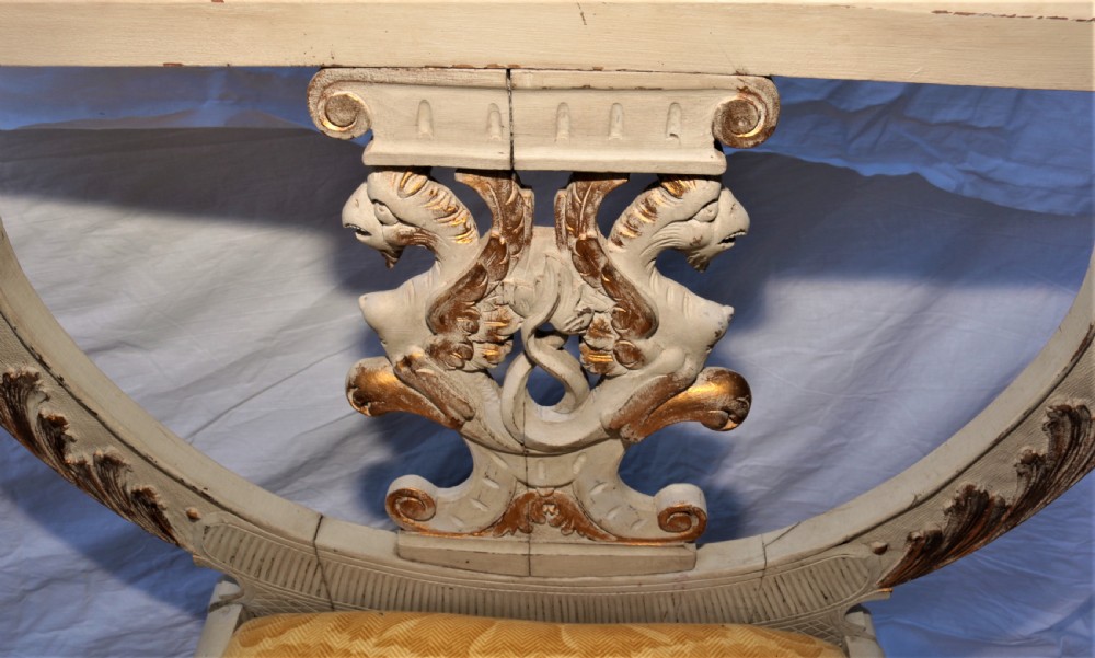 A pair of painted and carved giltwood Savonarola chairs with curved X-frames, ornate carved crests, and yellow patterned fabric seat cushions. View X