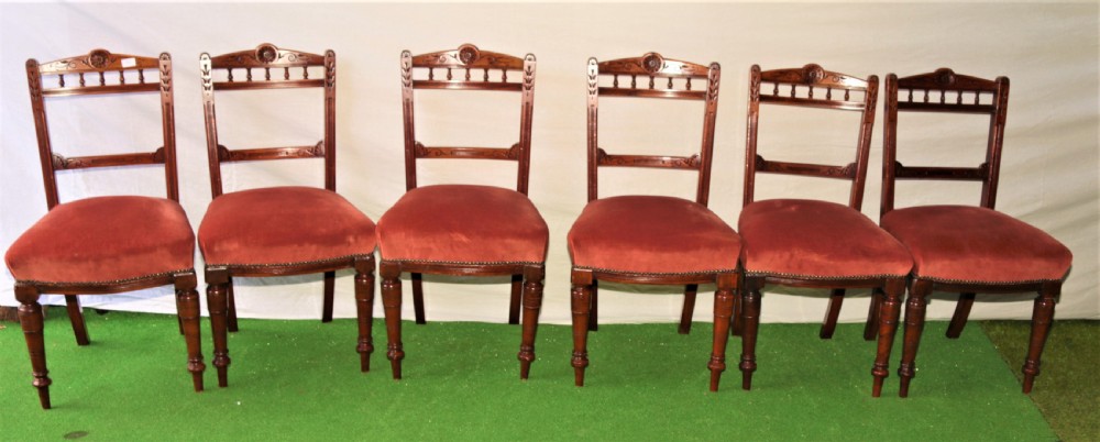 A set of six Victorian mahogany dining chairs featuring carved top rails with turned spindles, turned front legs, and red velvet padded seats.