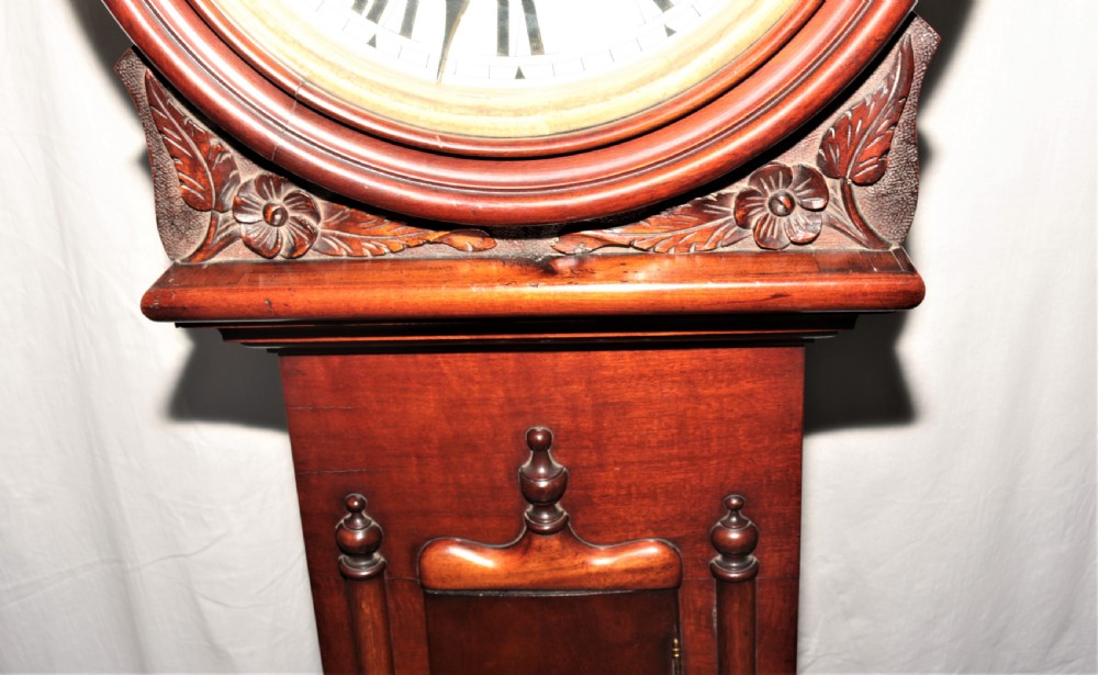 A Victorian flame mahogany drumhead longcase clock featuring a circular hood, Roman numeral dial, and a tapered trunk flanked by turned columns. View VI