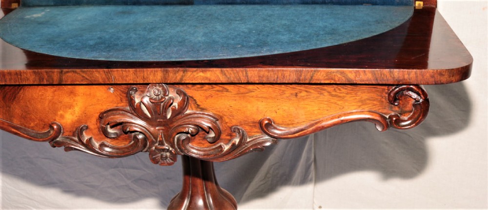 A William IV rosewood fold-over games table featuring an ornate carved apron, a sculpted central pedestal, and a four-legged carved base with brass castors. View III