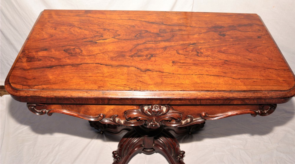 A William IV rosewood fold-over games table featuring an ornate carved apron, a sculpted central pedestal, and a four-legged carved base with brass castors. View VI