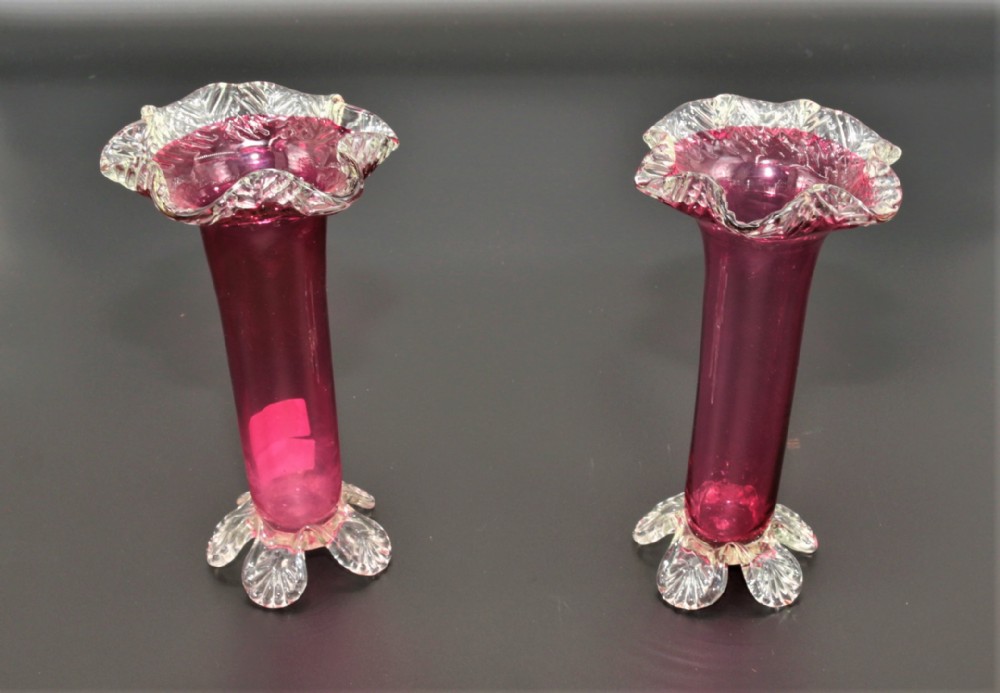A pair of Victorian cranberry glass trumpet vases featuring flared clear crimped rims and applied clear glass feet.
