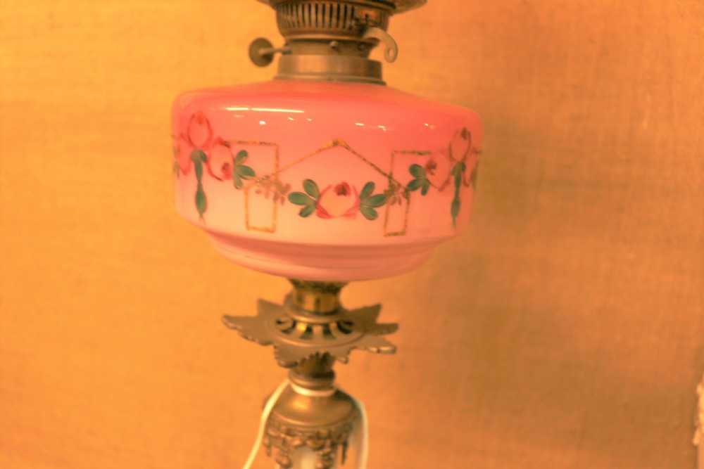 A tall Victorian oil lamp featuring a cast brass tripod base, a white reeded column, a pink hand-painted glass font, and a cranberry frosted glass shade. View VI