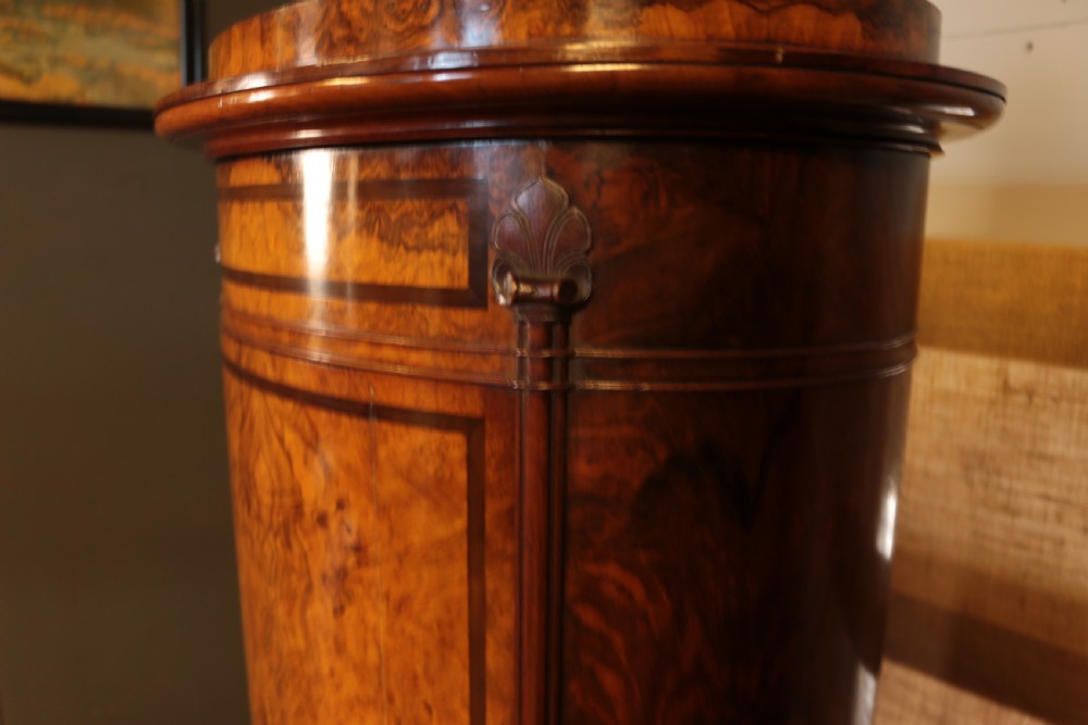 A tall cylindrical Victorian burr walnut pedestal cupboard with inlaid stringing details, a curved single door, and a moulded top. View V