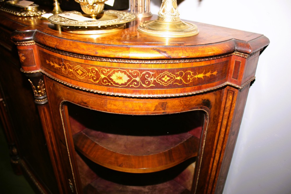 A Victorian burr walnut credenza featuring intricate floral marquetry inlay, gilt bronze mounts, a central panelled door, and curved glass side display compartments. View IV