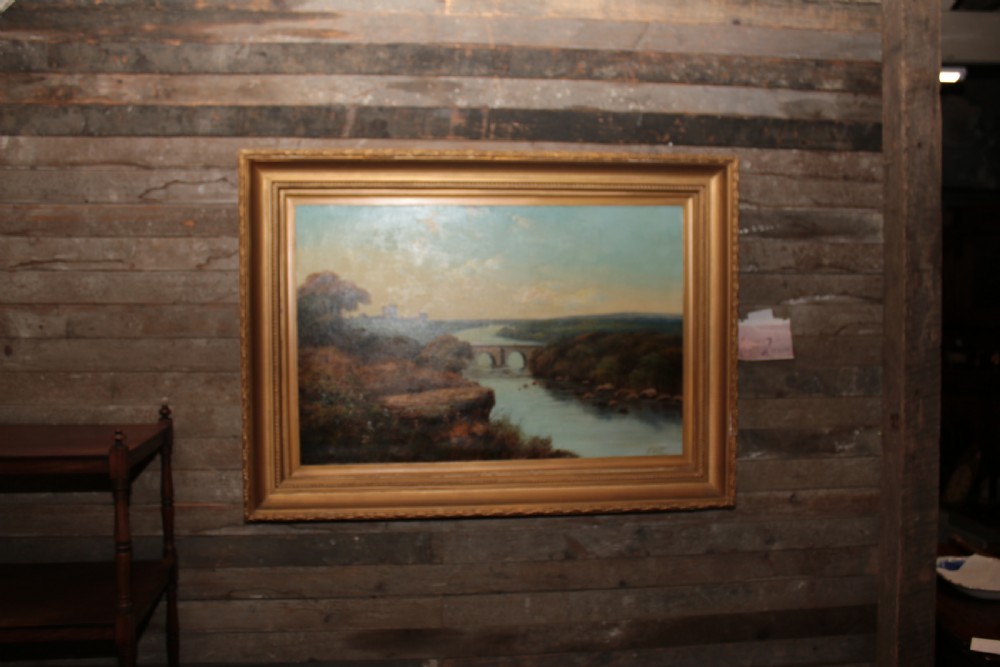 A framed landscape oil painting on canvas depicting Richmond Castle, a stone river bridge, and dense foliage beneath a soft blue sky. View IV