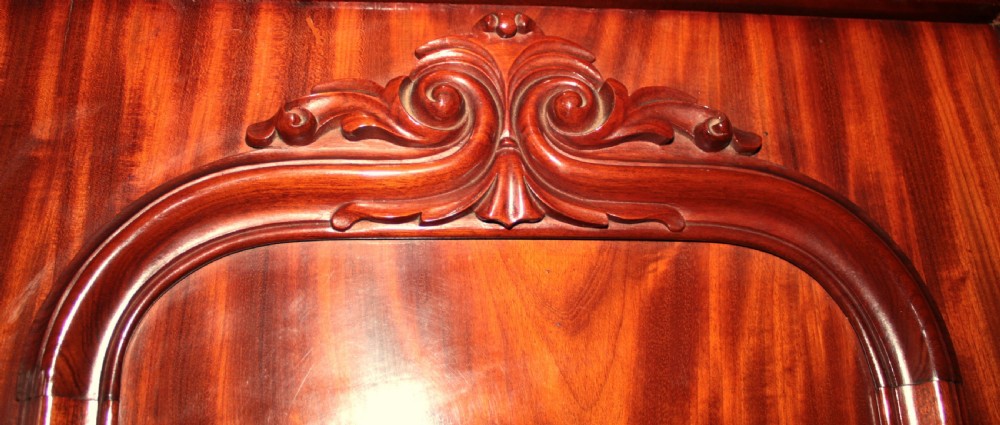 A large Victorian mahogany triple wardrobe featuring three arched panel doors with flame mahogany veneer figure, carved scroll crests, and a heavy moulded cornice. View IV