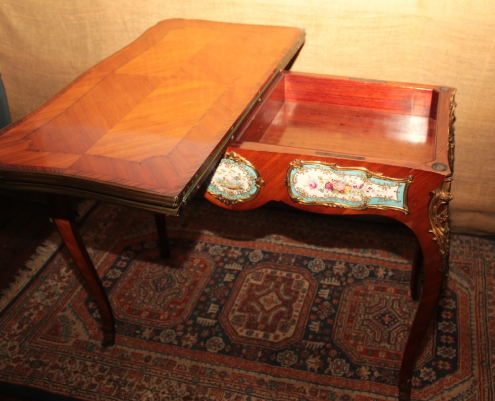 A mid-Victorian kingwood games table featuring cabriole legs, ornate gilt-bronze ormolu mounts, and inlaid porcelain plaques depicting floral scenes. View XV