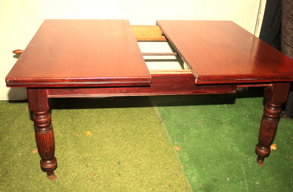 A late Victorian mahogany extending dining table featuring reeded turned legs on castors with a rectangular top. View VII