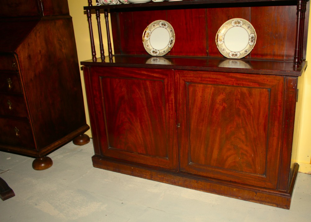 A Regency mahogany waterfall bookcase featuring open graduated shelves with turned spindle columns above a two-door base cupboard. View X