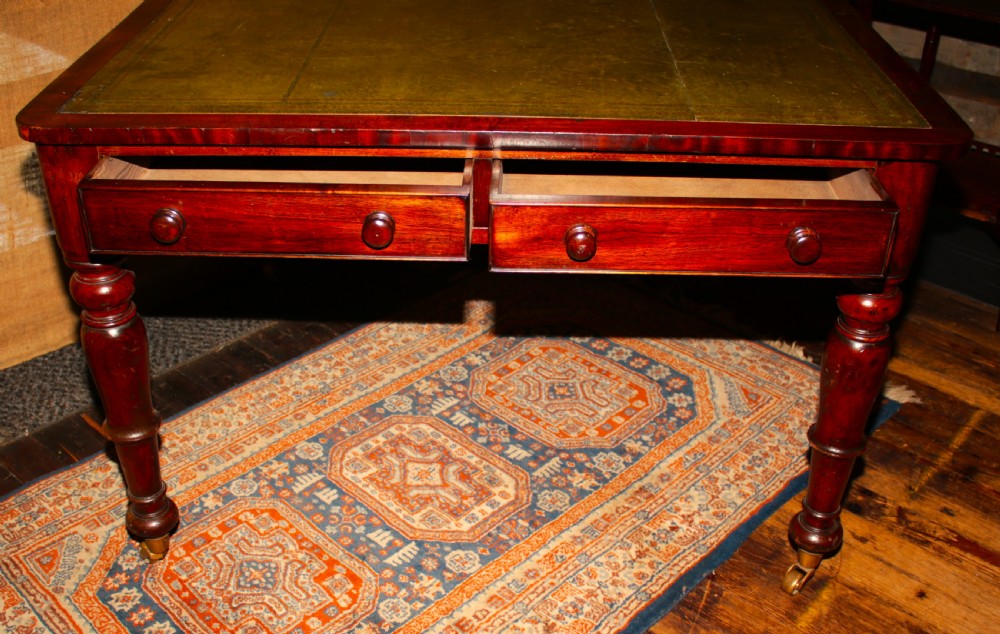 A William IV mahogany library desk featuring an inset leather top, two frieze drawers with turned wooden knobs, turned legs, and brass castors. View IV