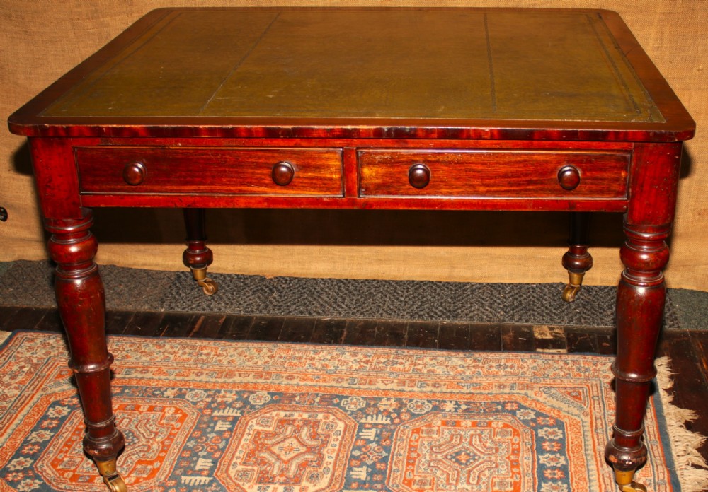 A William IV mahogany library desk featuring an inset leather top, two frieze drawers with turned wooden knobs, turned legs, and brass castors.