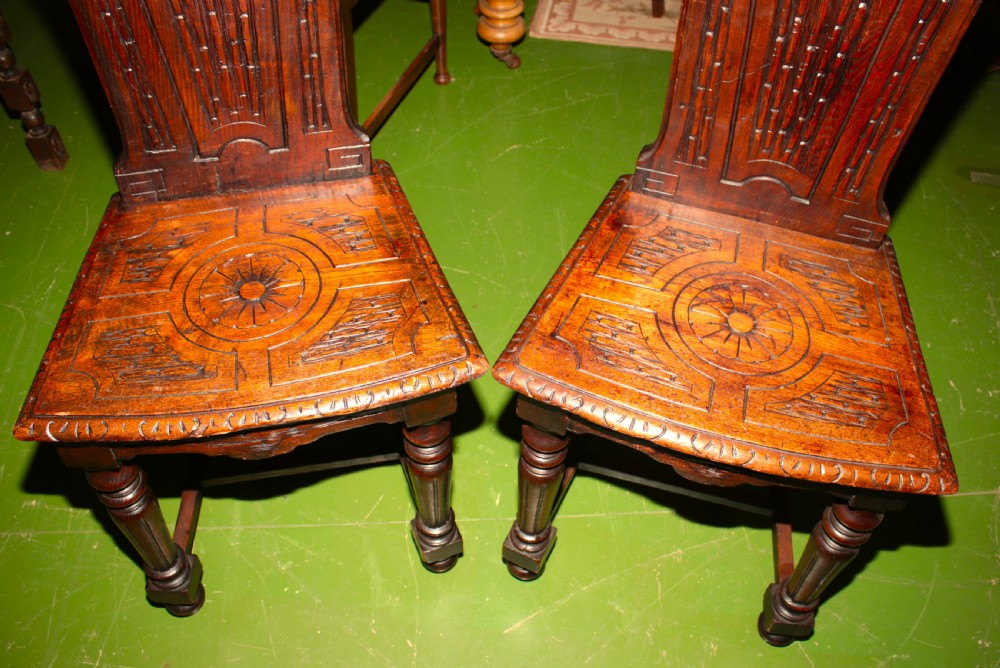 A pair of carved dark oak hall chairs featuring ornate back panels, carved wooden seats, and turned front legs. View III