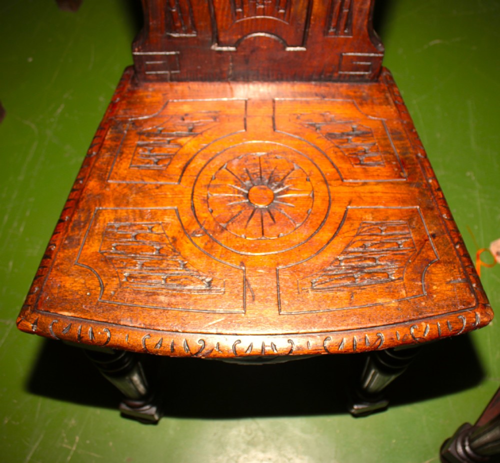 A pair of carved dark oak hall chairs featuring ornate back panels, carved wooden seats, and turned front legs. View IV