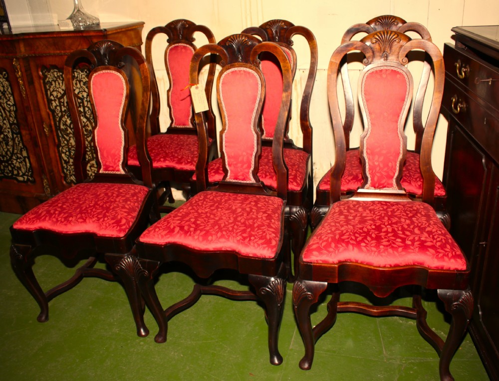 A set of six dark mahogany Queen Anne style dining chairs featuring carved shell crests and red patterned fabric upholstery.