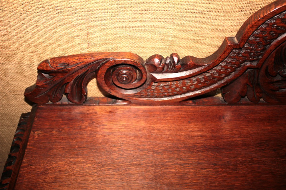 A dark carved oak side table featuring an ornate upstand with a mask motif, an intricately carved apron, and detailed legs. View III