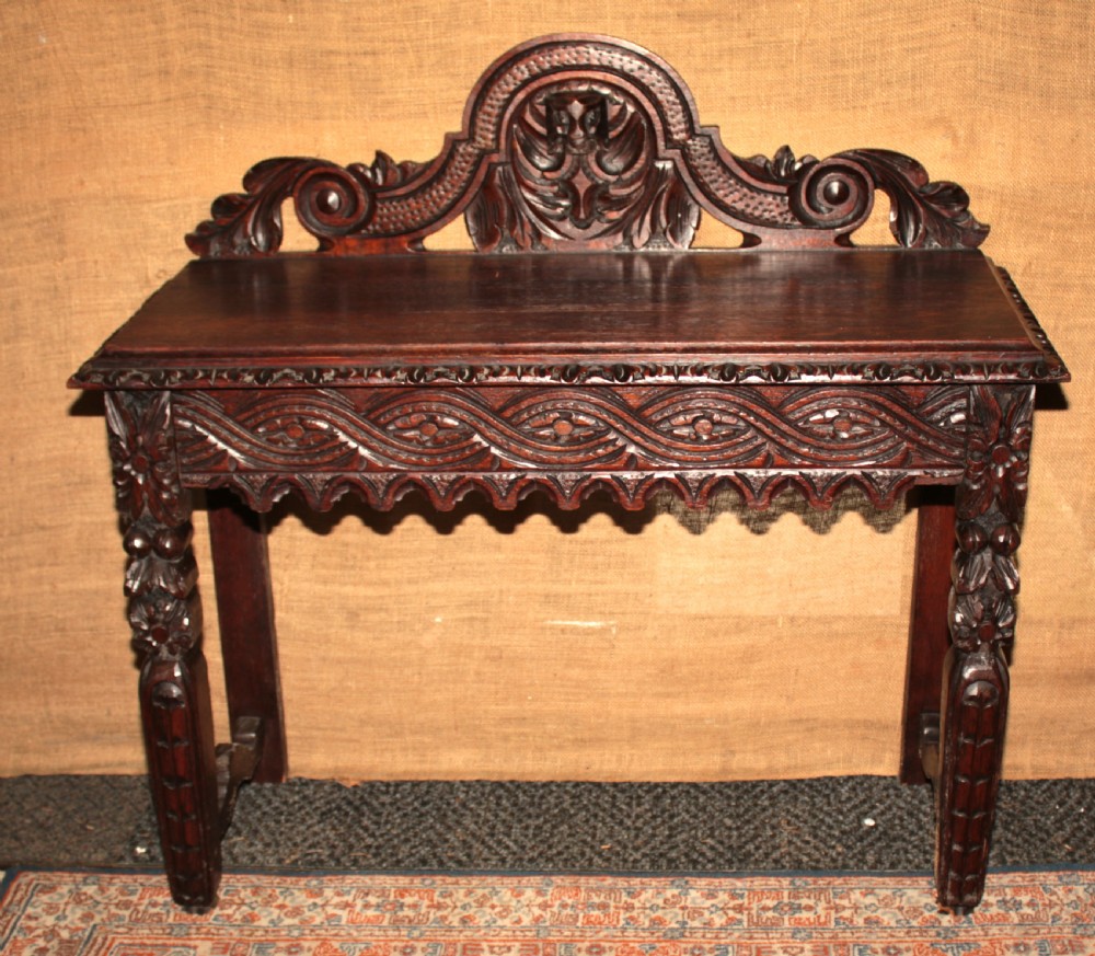 A dark carved oak side table featuring an ornate upstand with a mask motif, an intricately carved apron, and detailed legs. View IV