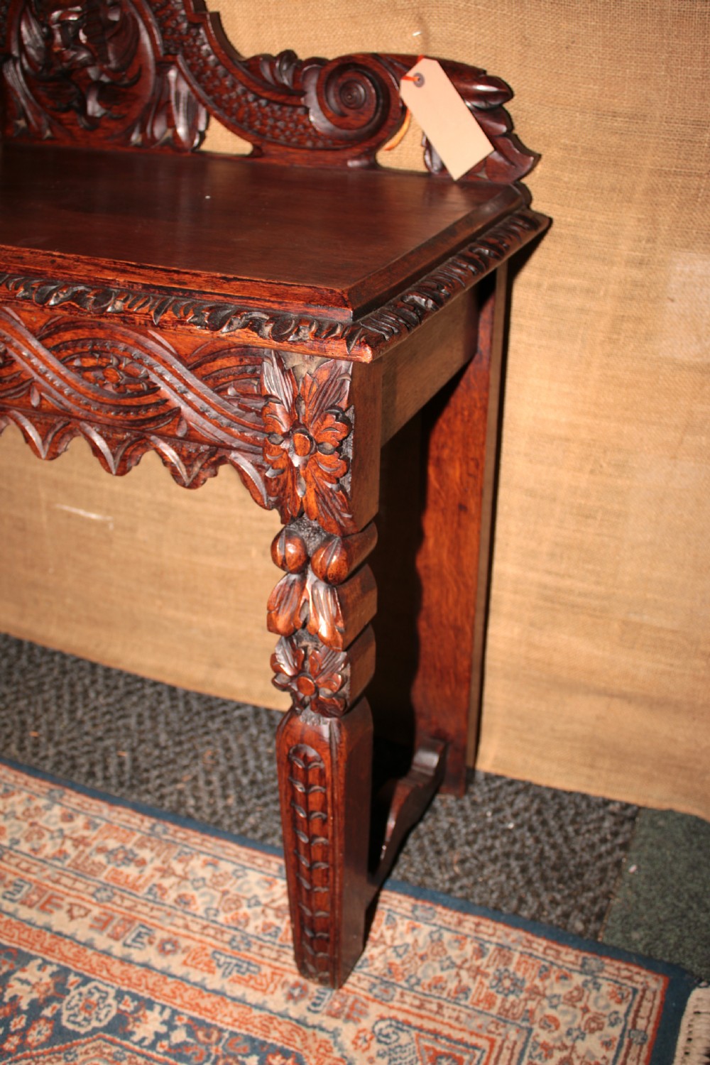 A dark carved oak side table featuring an ornate upstand with a mask motif, an intricately carved apron, and detailed legs. View V