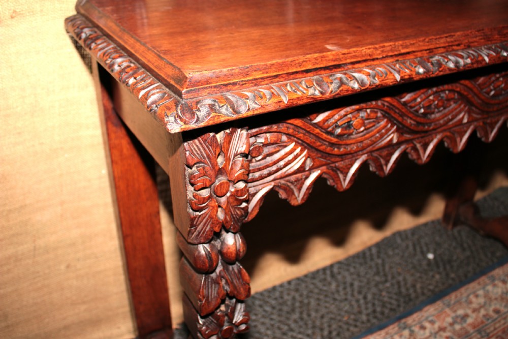 A dark carved oak side table featuring an ornate upstand with a mask motif, an intricately carved apron, and detailed legs. View VI