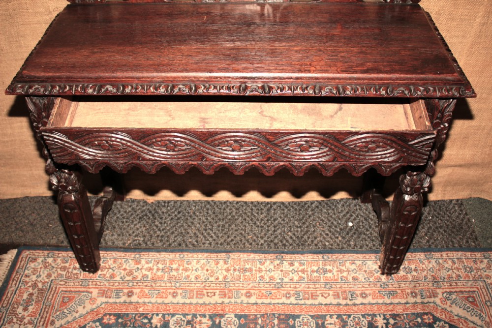 A dark carved oak side table featuring an ornate upstand with a mask motif, an intricately carved apron, and detailed legs. View IX
