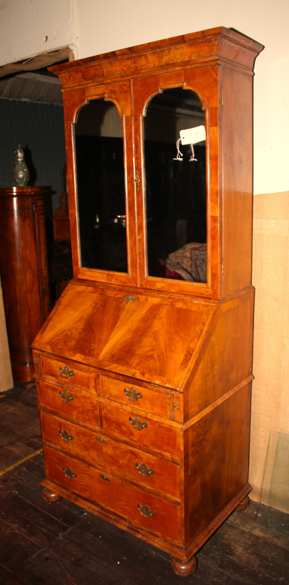 A George III walnut bureau bookcase featuring arched mirror-panel upper doors over a slant-front writing desk and multiple drawers with brass handles.