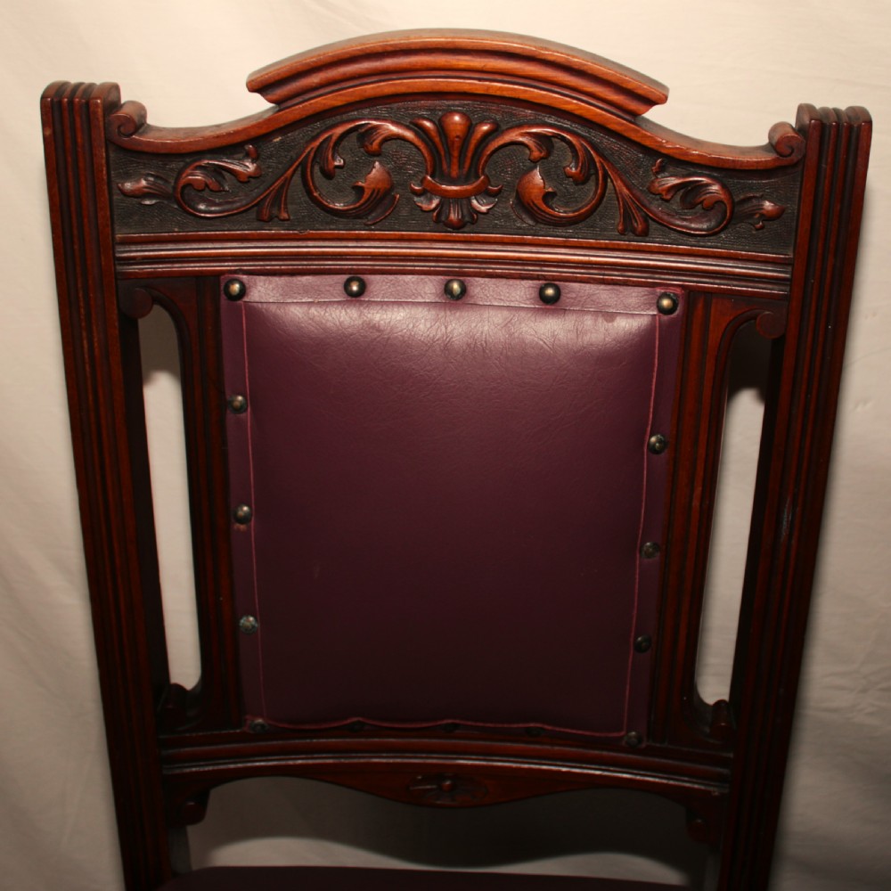 A set of six Victorian Irish mahogany dining chairs upholstered in deep plum leather with brass stud detailing, carved crests, and fluted front legs on castors. View III