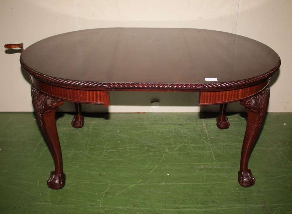An oval mahogany extendable dining table with carved cabriole legs, ball and claw feet, and a winding handle mechanism.