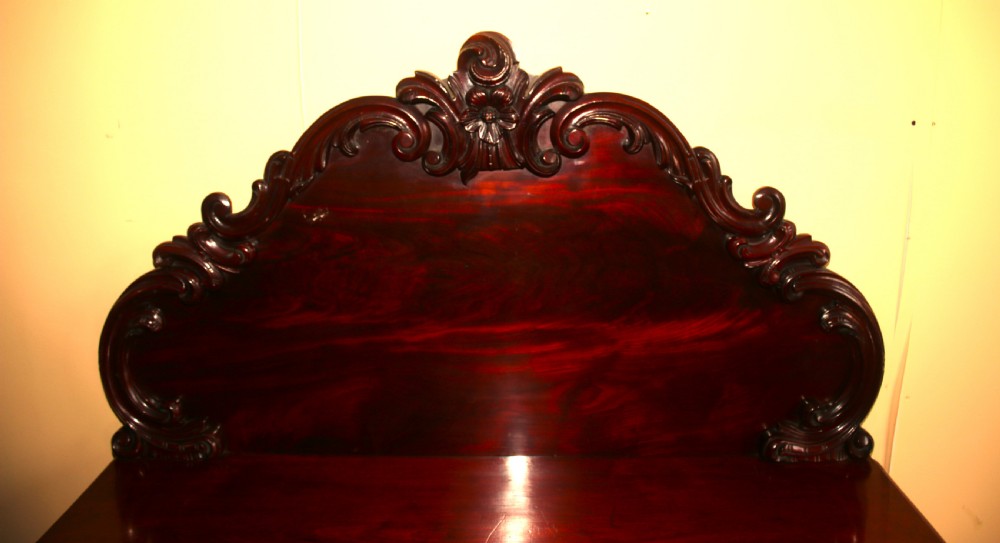 A Victorian mahogany two-door sideboard featuring a carved scrollwork backboard, flame mahogany panels, and a serpentine plinth base. View II