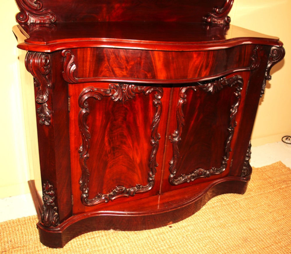 A Victorian mahogany two-door sideboard featuring a carved scrollwork backboard, flame mahogany panels, and a serpentine plinth base. View III
