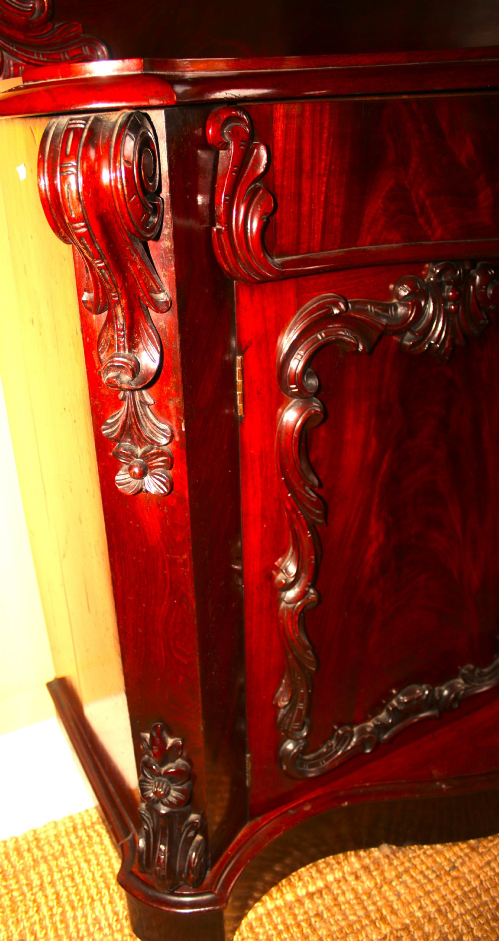 A Victorian mahogany two-door sideboard featuring a carved scrollwork backboard, flame mahogany panels, and a serpentine plinth base. View IV