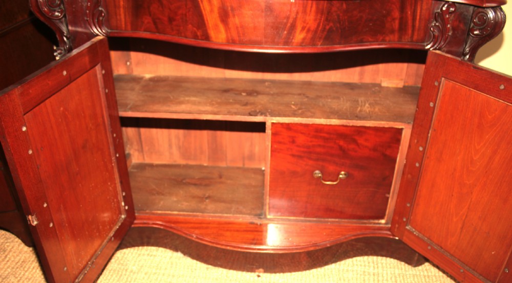 A Victorian mahogany two-door sideboard featuring a carved scrollwork backboard, flame mahogany panels, and a serpentine plinth base. View VIII