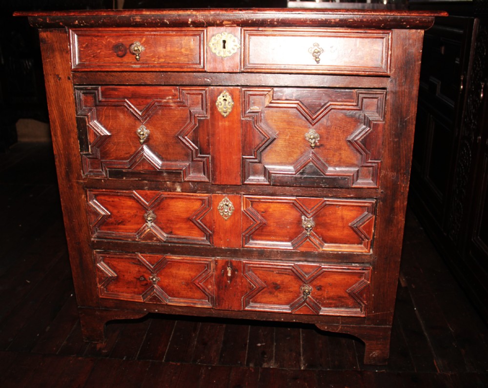 A late seventeenth-century dark oak chest of four drawers featuring raised geometric panel mouldings and brass drop handles. View III