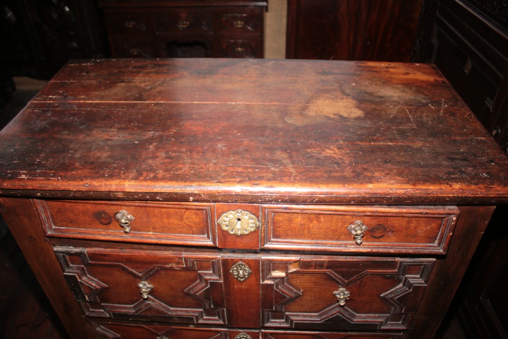 A late seventeenth-century dark oak chest of four drawers featuring raised geometric panel mouldings and brass drop handles. View V