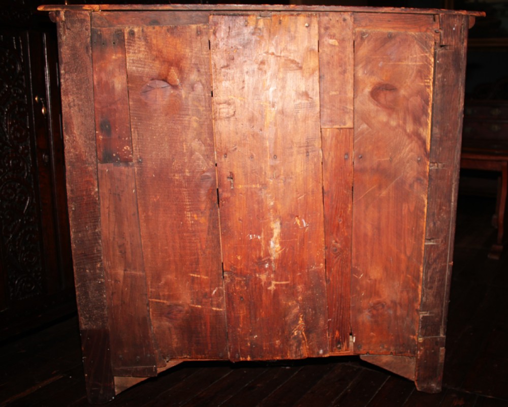 A late seventeenth-century dark oak chest of four drawers featuring raised geometric panel mouldings and brass drop handles. View VII