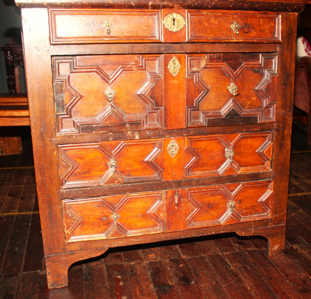 A late seventeenth-century dark oak chest of four drawers featuring raised geometric panel mouldings and brass drop handles. View XI