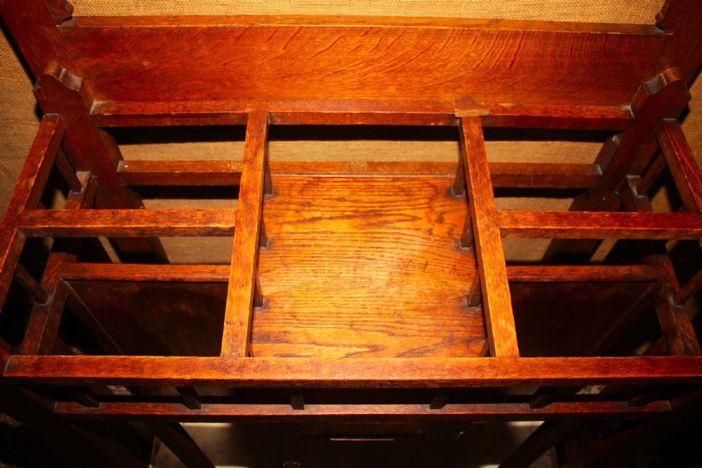 An Arts and Crafts oak hall stand featuring a central square mirror, metal coat hooks, umbrella drip trays, and a lower storage cupboard. View III
